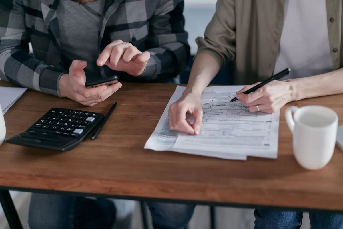Two people at a wooden desk working through tax paperwork with a calculator and pen