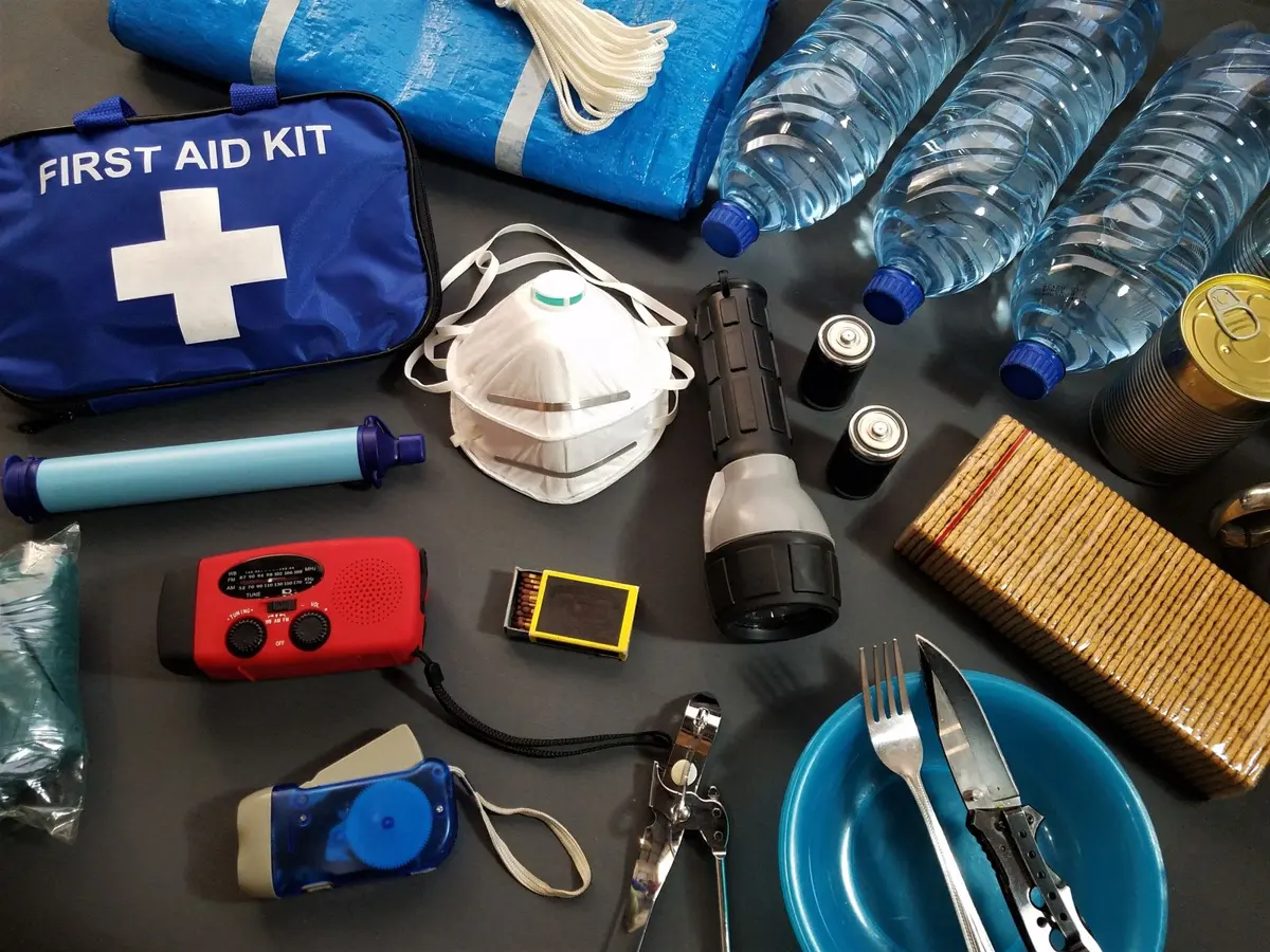 Emergency kit laid out with a first aid kit, water bottles, torch, batteries, masks and a radio