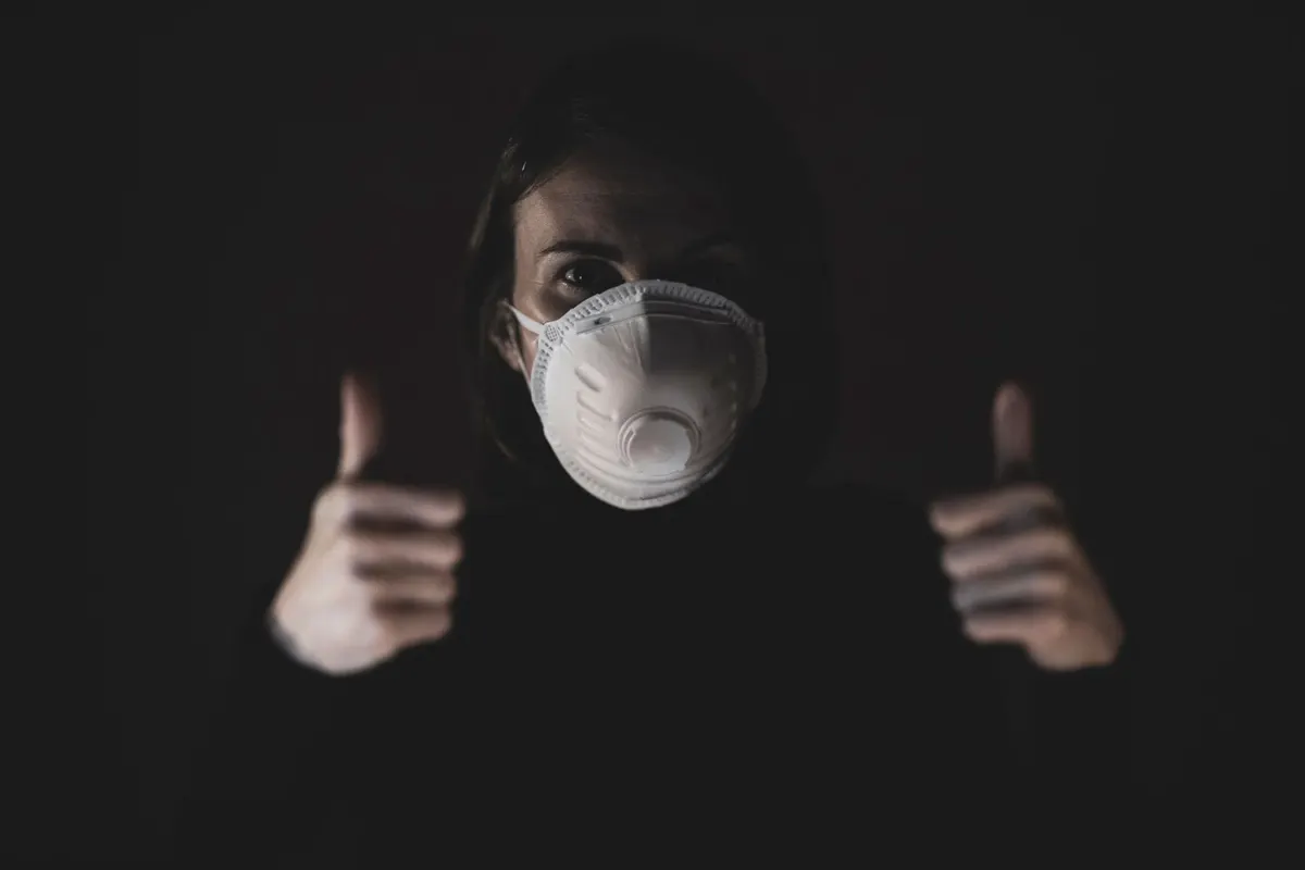 A person wearing a white N95 respirator mask giving a thumbs-up